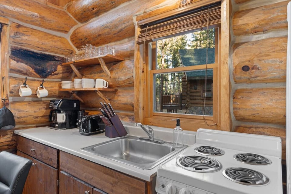 Cabin kitchen view of pine-covered hills and neighboring log homes. Blending rustic living with serene forest surroundings.