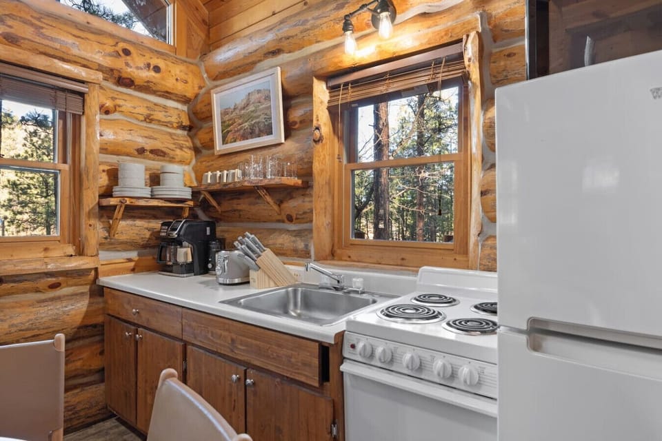 Cabin kitchen with views of pine-covered hills and nearby log homes—where rustic charm meets peaceful forest scenery.