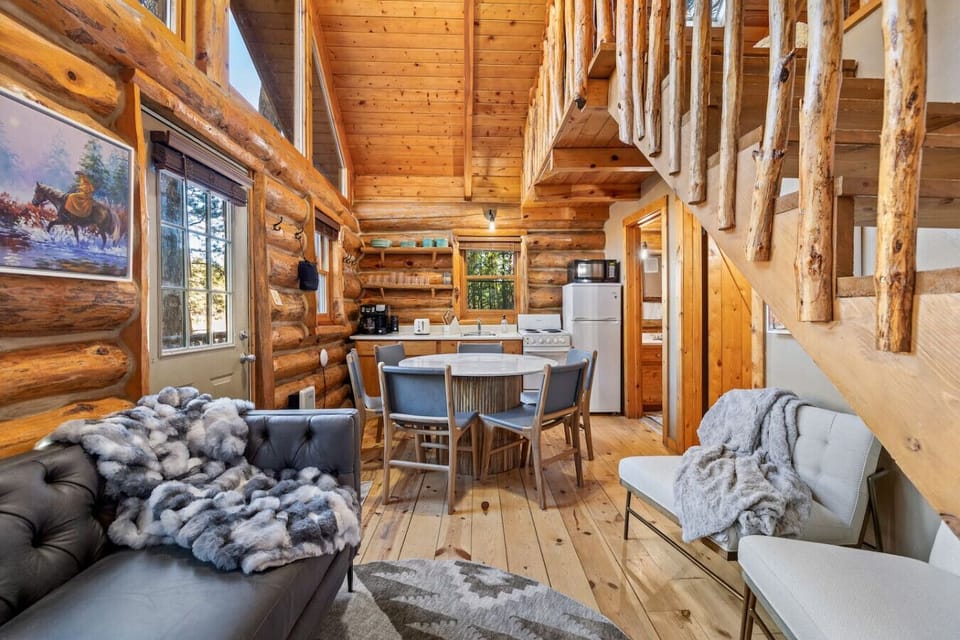 Open concept log cabin interior with dining table, kitchen, and loft stairs in the Black Hills, South Dakota.