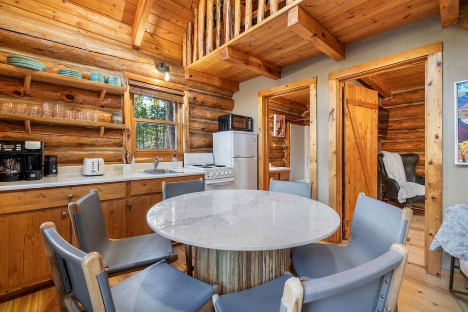 Gather around the dining table in the open concept main floor with a full kitchen, loft above, and warm cabin finishes.