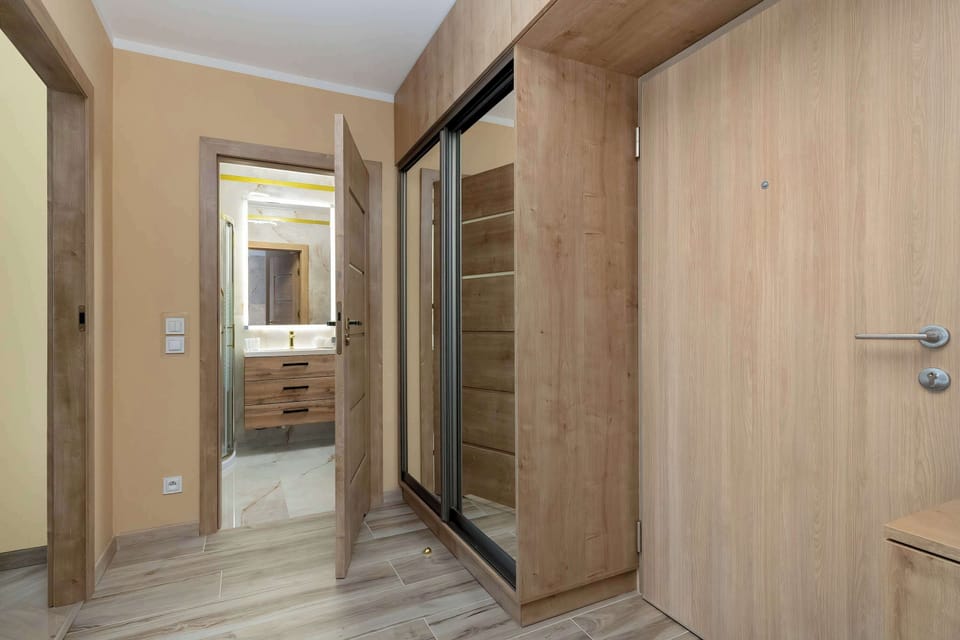 The hallway features a large, mirrored sliding-door wardrobe that visually expands the corridor. Light-colored wooden doors lead to the bathroom and other rooms, maintaining a consistent aesthetic.