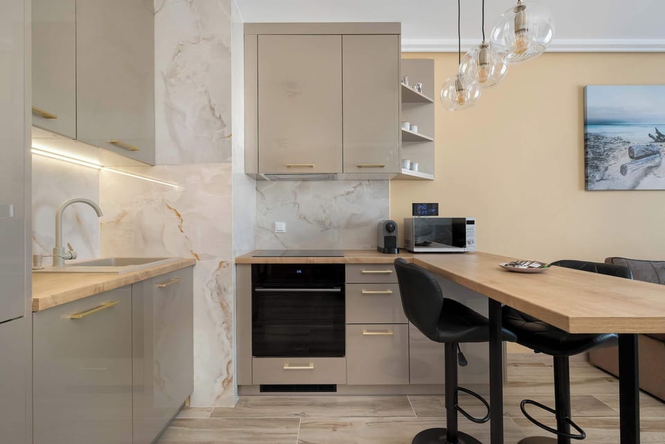 A modern kitchenette is equipped with sleek grey cabinetry and light marble-patterned backsplashes. A wooden breakfast bar with black stools provides a convenient spot for dining or working.