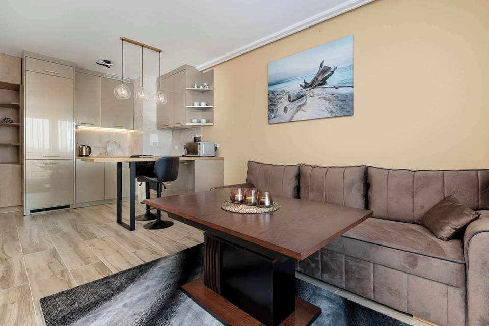 A stylish brown sofa faces a wooden table, creating a perfect nook for morning coffee or casual meals. On the wall, a piece of framed art depicting a coastal scene adds a touch of serenity to the decor.