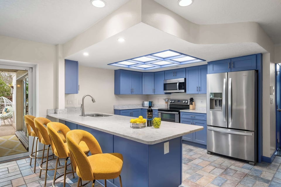 Modern kitchen w/ stainless steel fridge, island seating & vibrant yellow accents.
