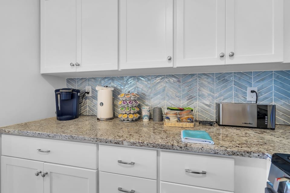 Bright kitchen nook with granite counters, coffee station, and blue tile backsplash