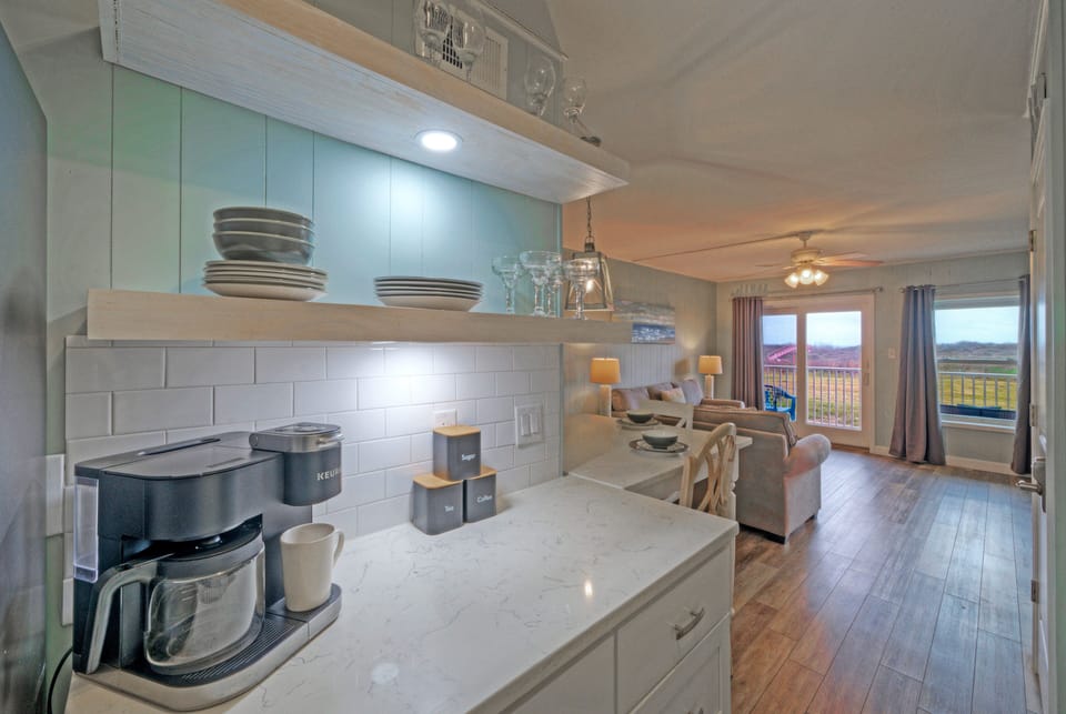 Bright kitchen with stainless appliances, quartz countertops, and open shelving—ready for everything from quick coffee to full coastal dinners.