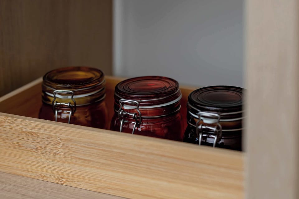 A wooden organizer inside a cabinet neatly stores glass jars with dark lids. This highlights the organized and practical storage solutions available throughout the apartment.