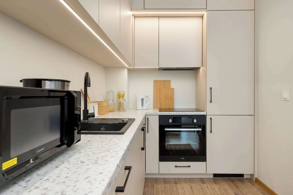 The kitchen view emphasizes the clean lines of the handleless white cabinetry and the contrast with black fixtures. A large refrigerator is seamlessly integrated into the furniture for a sleek look.