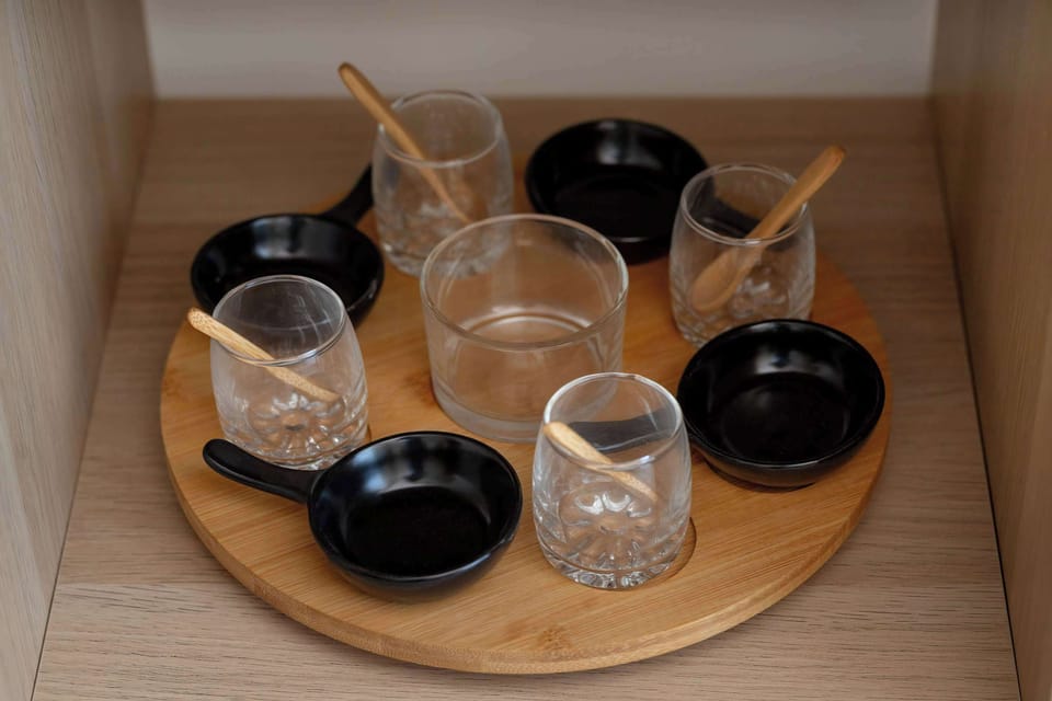 A wooden tray holds a set of stylish glassware, including transparent cups and small black bowls. This thoughtful detail suggests a well-equipped kitchen ready for guests to enjoy a drink.