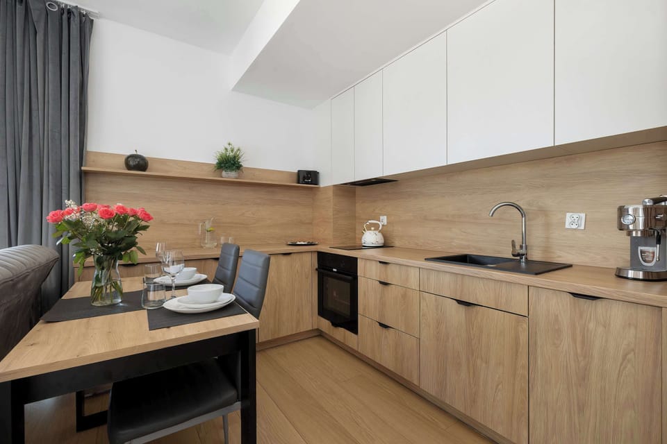 A wider kitchenette view showing a dining table and cabinetry extending along the wall. Neutral colors and wood textures dominate the design.