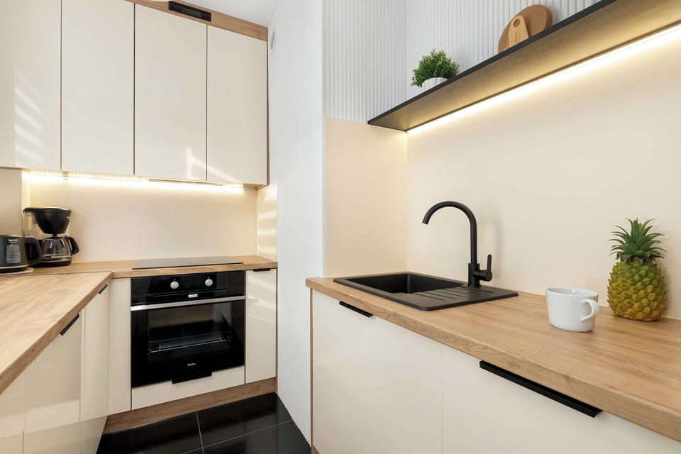 Another angle of the compact kitchen with under-cabinet lighting illuminating the countertop. A sink and faucet are visible beneath the cabinets. The design emphasizes simplicity and efficiency.