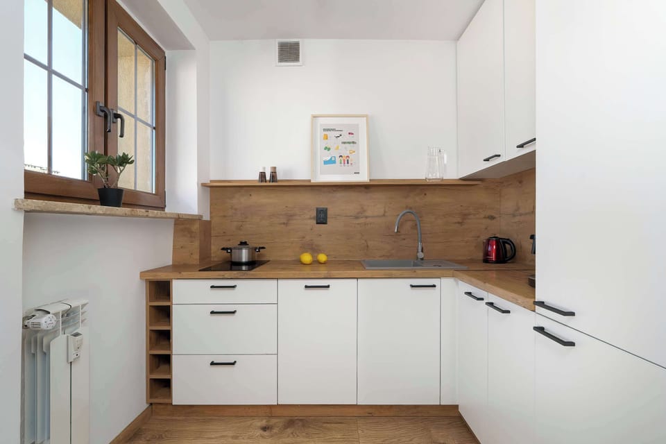 A second view of the kitchen with white cabinets and wooden countertops. A small window above the sink allows natural daylight to brighten the space. The layout is compact but practical.