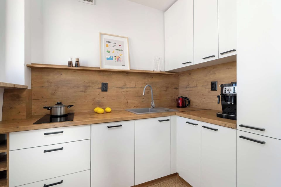 A compact kitchen designed with white cabinets and wooden countertops. Built-in appliances and a small cooking area create a practical workspace for preparing meals. A few small decorations and fruit add a welcoming feel.
