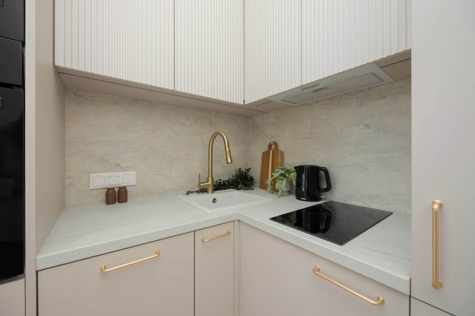 A small kitchen corner with white cabinets and a sink. Soft lighting highlights the clean surfaces. The design appears simple and functional.