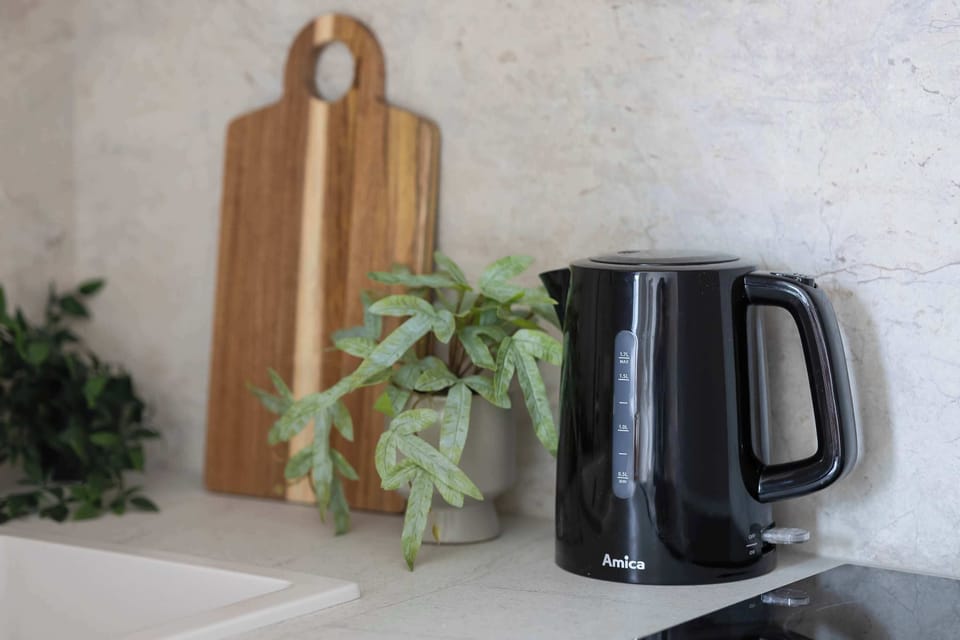 A kitchen countertop with a kettle, cutting boards, and a small plant. Light cabinetry and backsplash tiles create a cohesive look. The styling feels practical yet decorative.