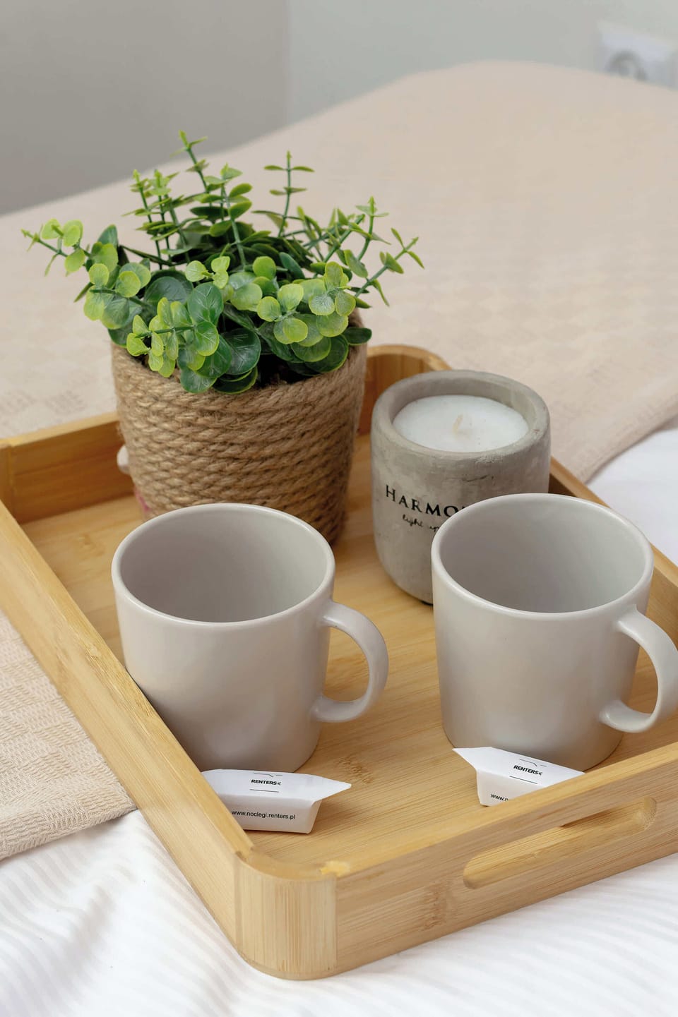 A wooden tray on the bed containing two grey mugs and a small potted plant. This detail emphasizes the welcoming and homely feel of the apartment.