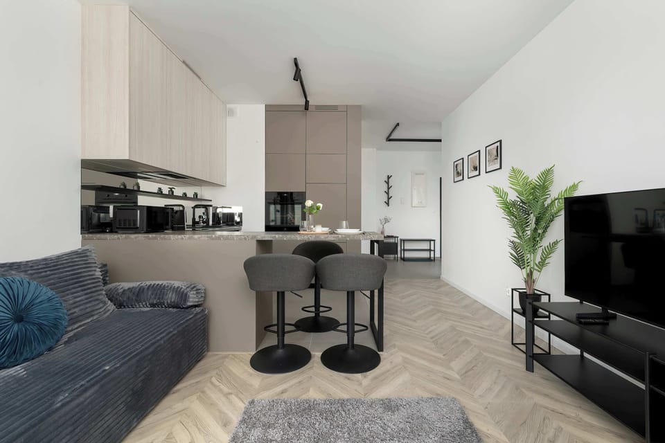 An open-plan living space with a modern kitchenette. Dark chairs contrast with the light interior. The layout looks functional and stylish.