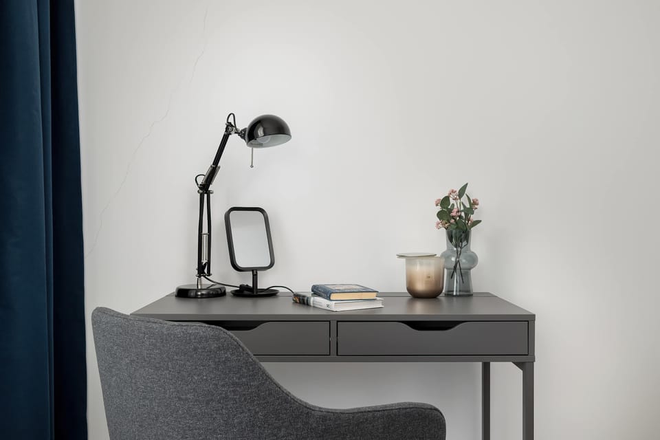 A small desk area with a modern chair and lamp. The setup is suitable for working or studying. The design is simple and practical.