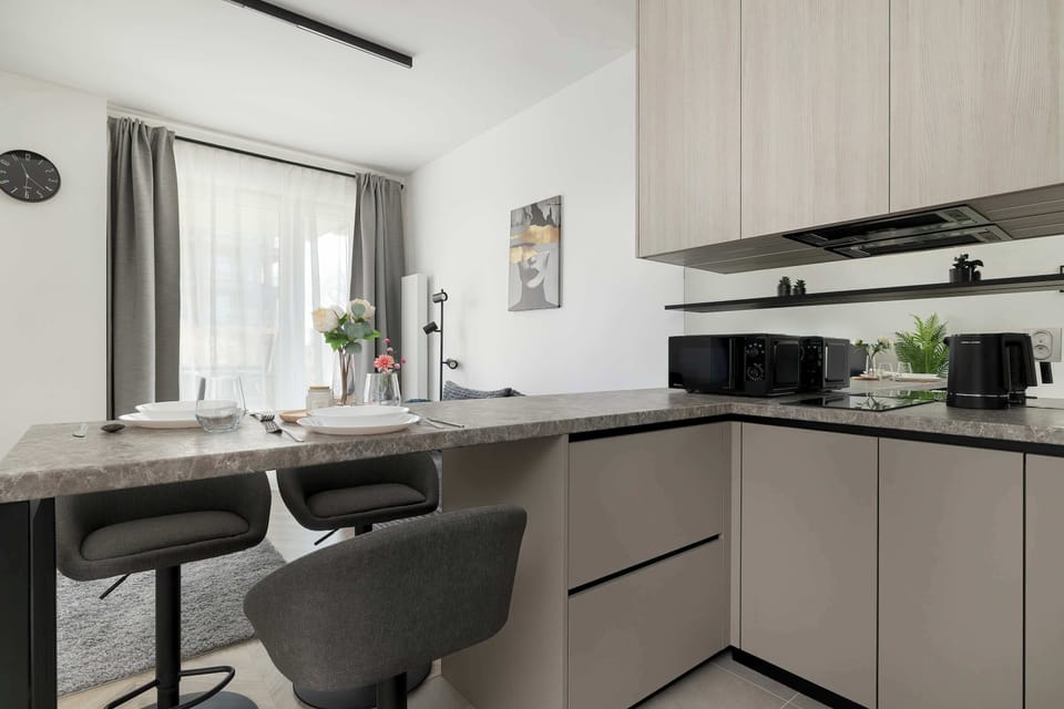 A modern kitchenette with beige cabinets and built-in appliances. A small dining counter with stools adds practicality. The design is compact and efficient