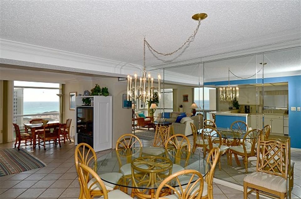 Your spacious oceanfront retreat features an open-plan living space where elegant chandeliers cast warm light over coastal-themed dining and lounging areas.