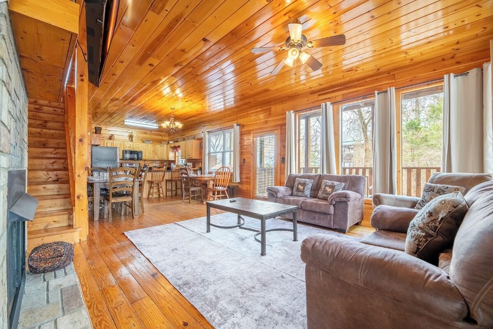 Relax in your spacious cabin living room with soaring wood ceilings, comfy leather seating, and peaceful forest views through large windows.