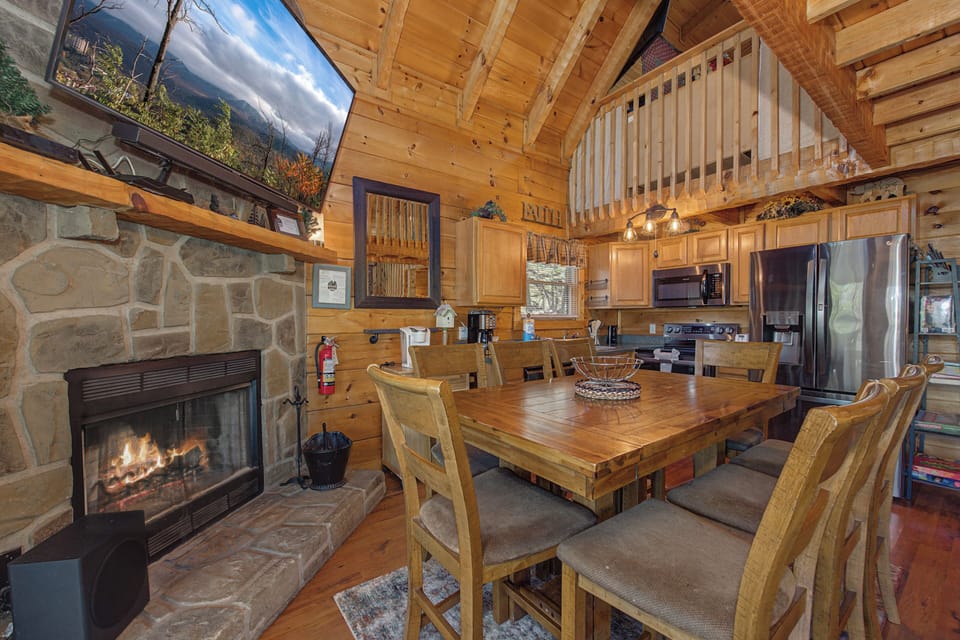 Your cozy cabin retreat features rustic wood beams, a crackling stone fireplace, and a welcoming dining space perfect for gathering.