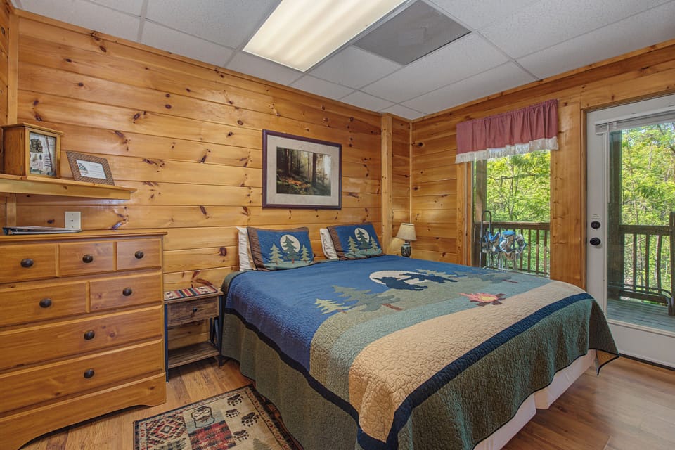 Wake up in this cozy cabin bedroom with warm wood walls, comfortable bedding, and your own private balcony overlooking the trees.