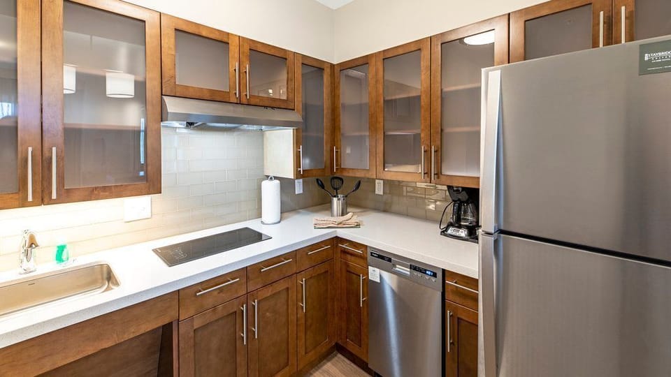 A closer look at the kitchen shows wooden cabinets, a refrigerator, tile backsplash, and built-in appliances.