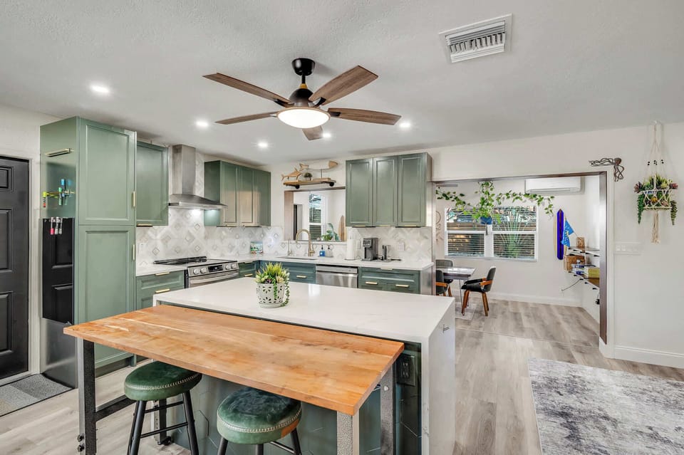 Modern kitchen with green cabinetry, a large island, and a wooden breakfast bar.