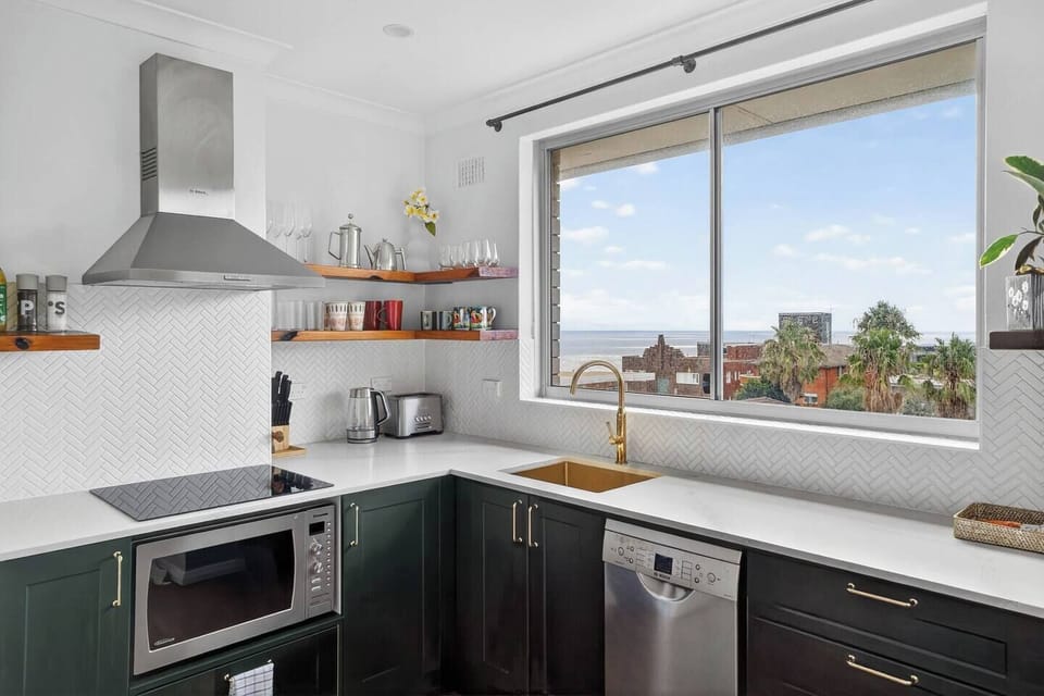 Prepare breakfast by the window as treetops and sea glimpses frame the kitchen in soft coastal light.