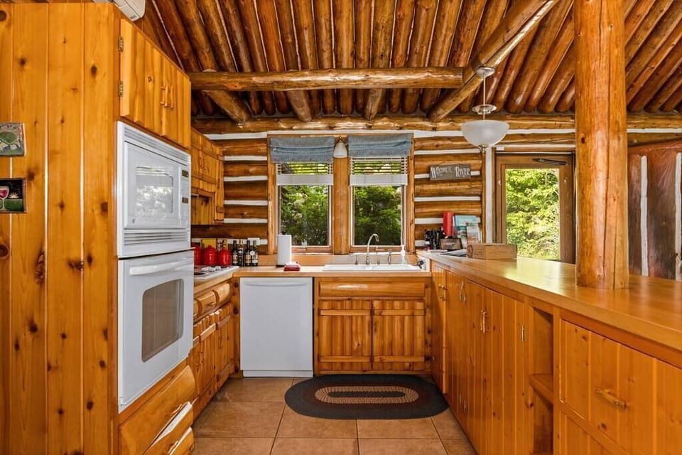 Rustic log cabin kitchen with warm wood cabinetry, full appliances, ample counter space, and peaceful wooded views.
