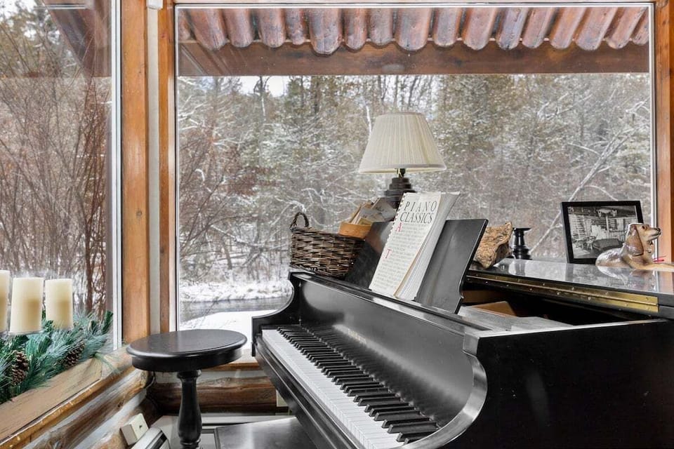 Cozy piano nook with snowy woodland views, warm cabin details, and peaceful charm for a relaxing getaway.