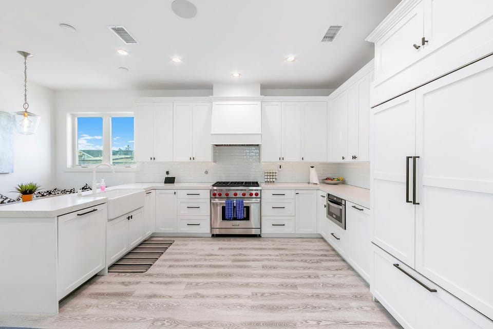 Sleek, all-white kitchen with top-of-the-line appliances, ample counter space, and bar seating at the island — perfect for cooking and gathering.