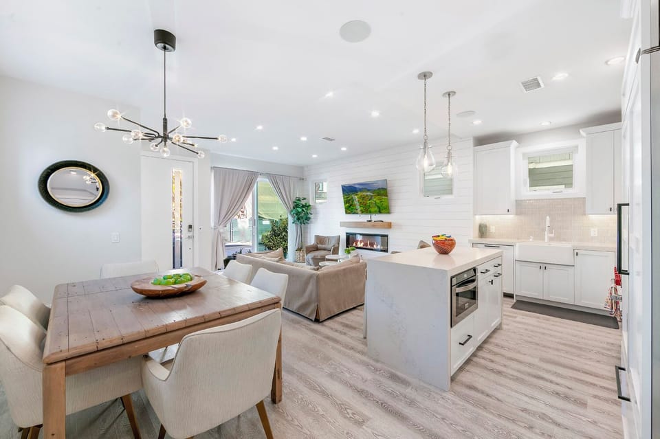 The dining area and kitchen island in Unit A — a bright, central gathering spot with pendant lighting, bar seating, and a stylish round mirror accent.