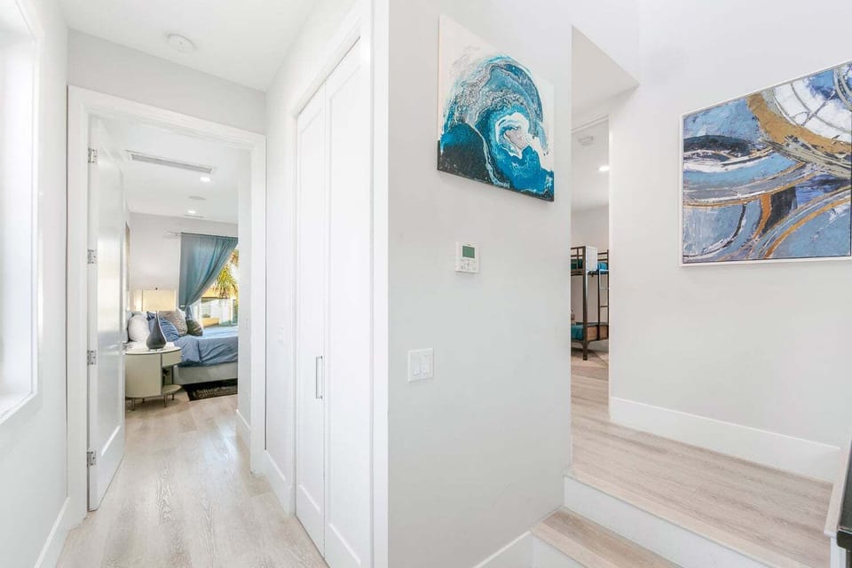 A sun-drenched hallway featuring neutral flooring and contemporary blue-toned artwork. This clean transition space leads into the serene bedrooms, continuing the home's modern coastal aesthetic.
