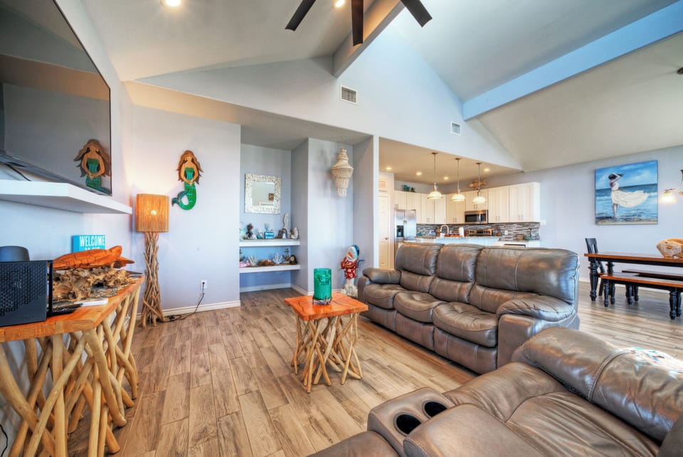Bright, coastal living room with vaulted ceilings, comfy recliners, and bay-view balcony access.