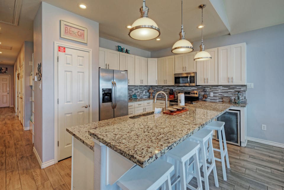 Spacious, fully stocked kitchen with granite island seating, stainless steel appliances, and bright pendant lighting.