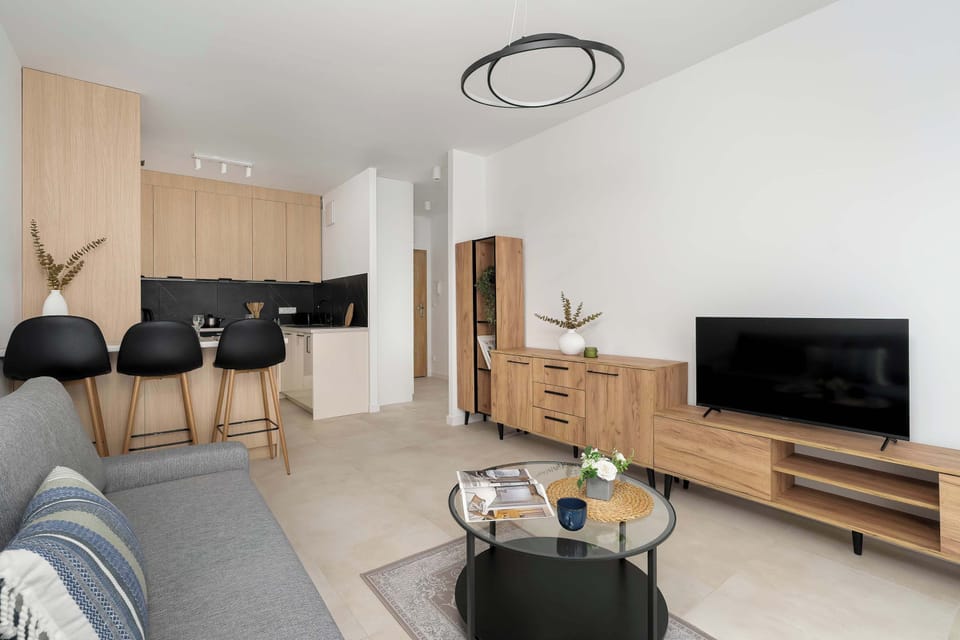 The interior layout shows the connection between the living room and the kitchenette. Black bar stools provide a sleek contrast to the light wooden cabinetry.