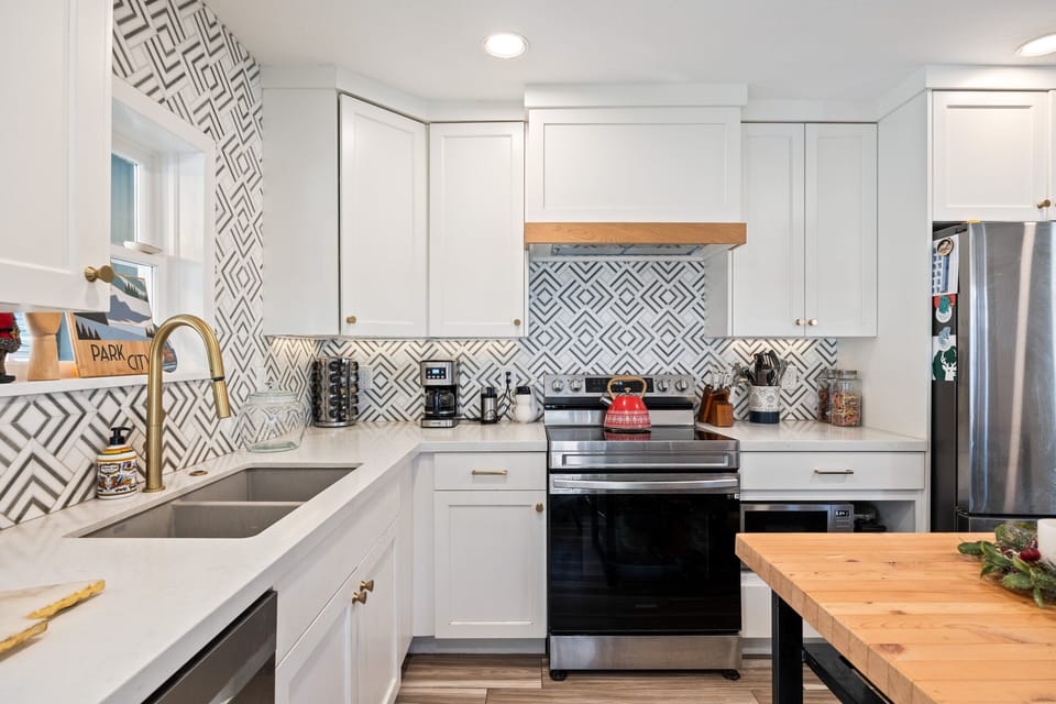 Fully updated kitchen with stainless steel appliances, sleek white cabinetry, and patterned tile backsplash.