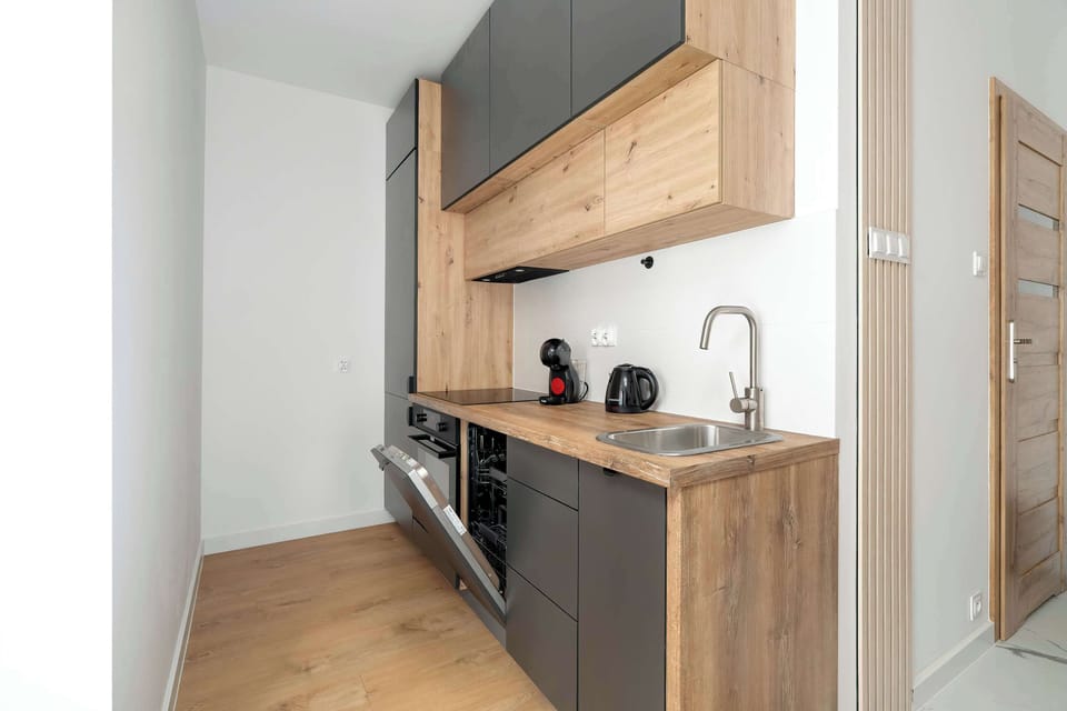Another angle of the kitchenette featuring wooden cabinets, a sink, stovetop, and light-colored walls.