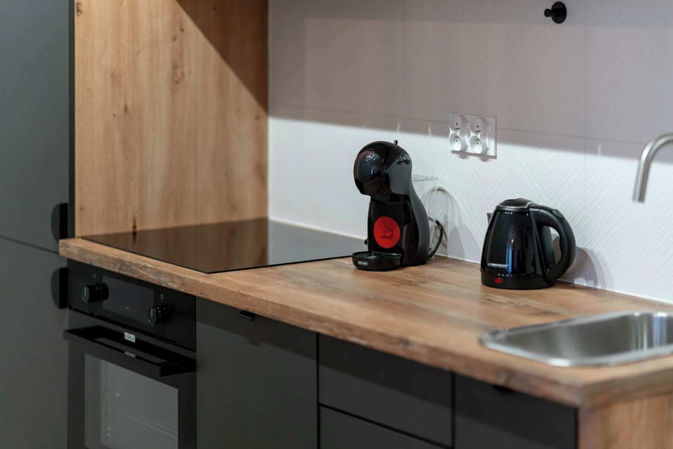 A close-up of the kitchen counter with a coffee machine, kettle, stovetop, and wooden backsplash.