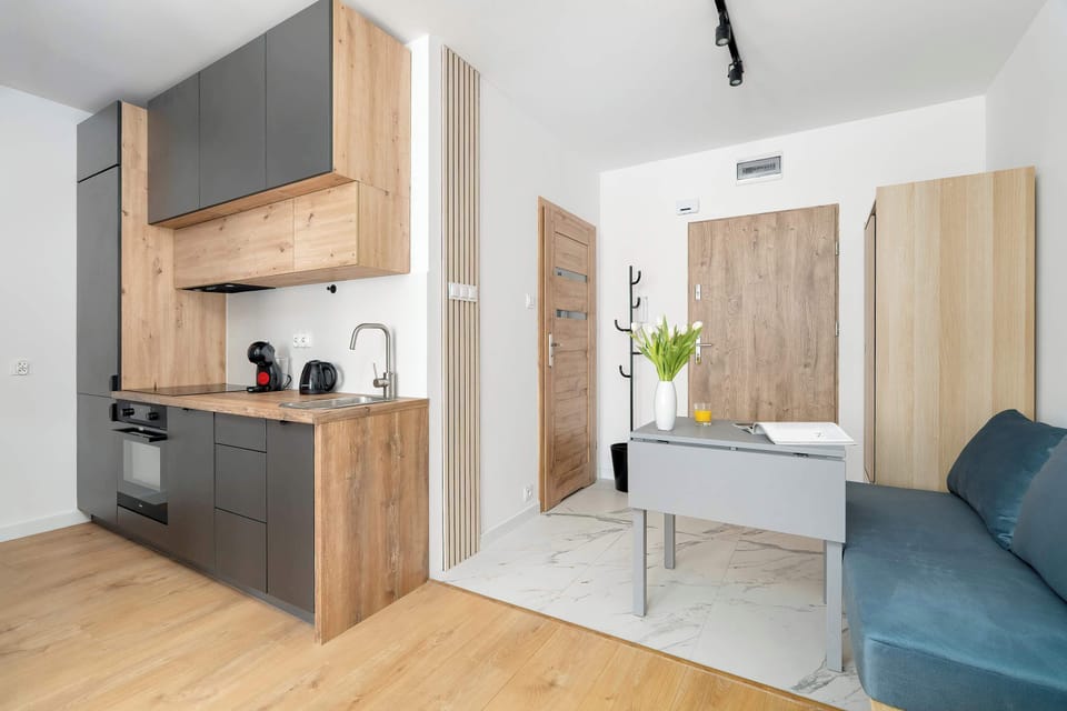 A compact kitchen and entryway area with light wood cabinets, a refrigerator, and a glimpse of the living room beyond.