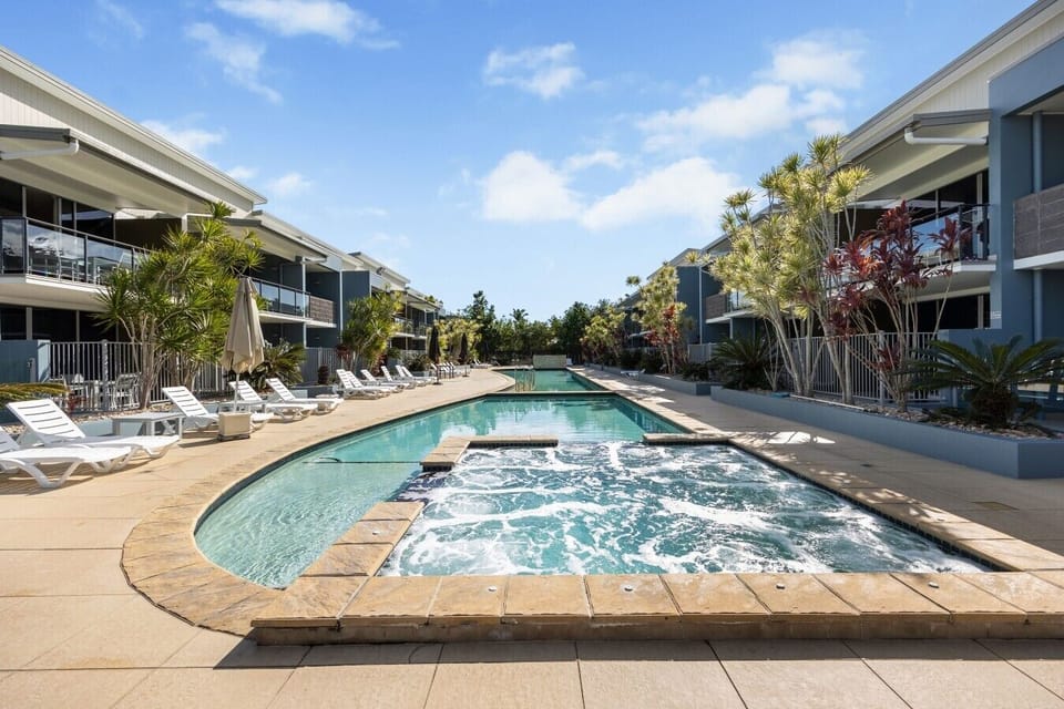 Sparkling resort-style pool and spa surrounded by palm trees and sun loungers — your daily holiday ritual starts here.