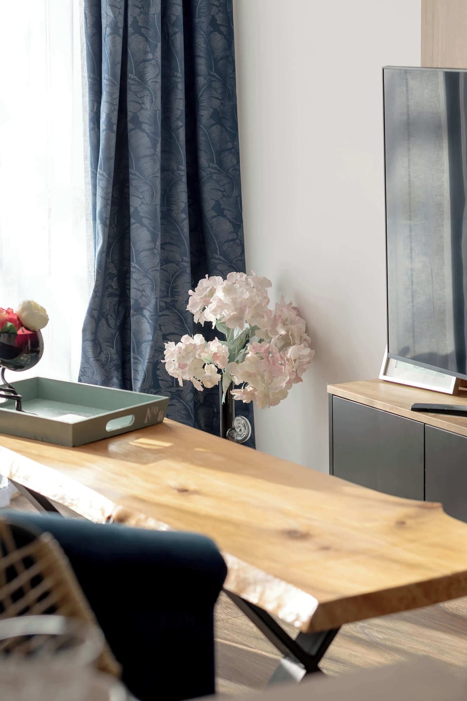 A close-up of a wooden dining table decorated with a small vase of flowers. The view extends toward the living area, emphasizing the home's cohesive design.