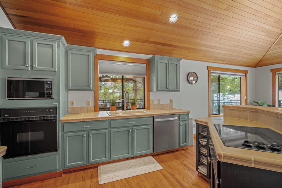Your fully equipped kitchen features sage-green cabinets and warm wood ceilings, perfect for preparing meals while enjoying lake views through the window.