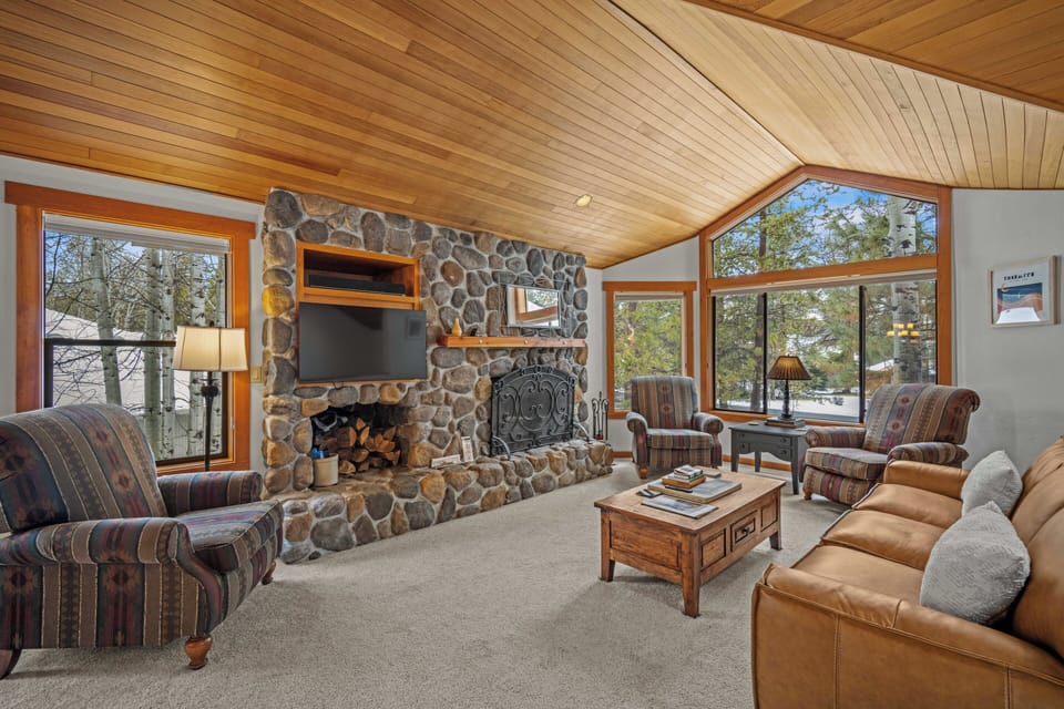 Sink into plush seating by the stone fireplace while natural light streams through expansive windows, creating your perfect mountain retreat sanctuary.