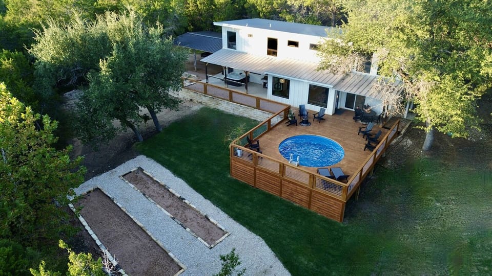 Modern retreat nestled among mature trees featuring an elevated deck with swimming pool and outdoor dining space.
