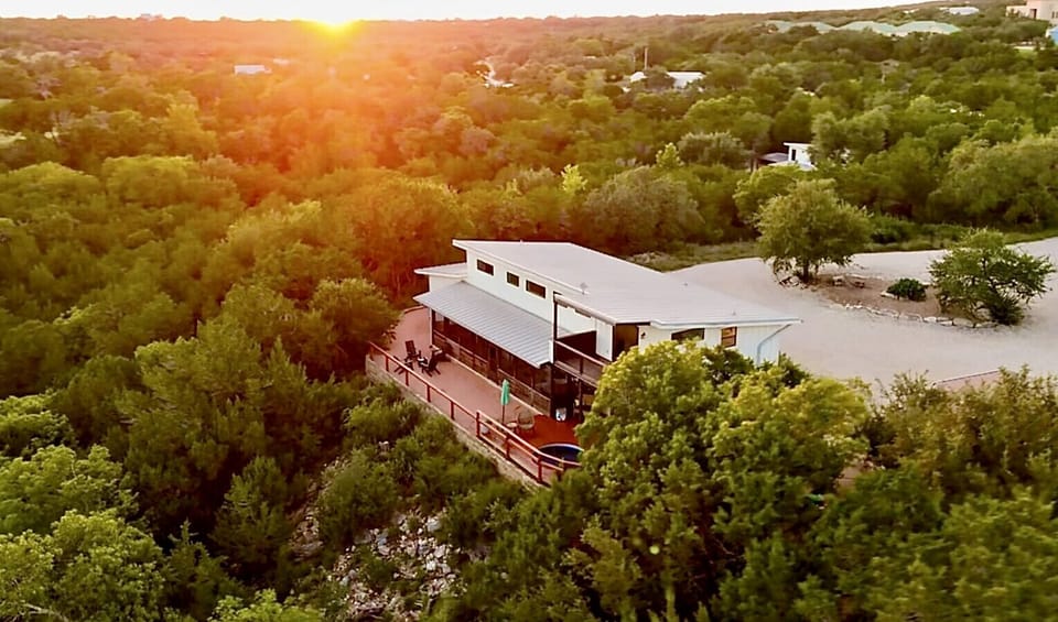 Modern retreat nestled among rolling hills at golden hour, featuring contemporary architecture surrounded by lush Texas Hill Country landscape.