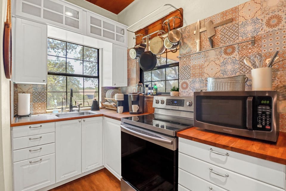 Your fully-equipped kitchen invites you to cook and gather, with warm wood countertops, charming patterned tile, and morning sunlight streaming through the windows.