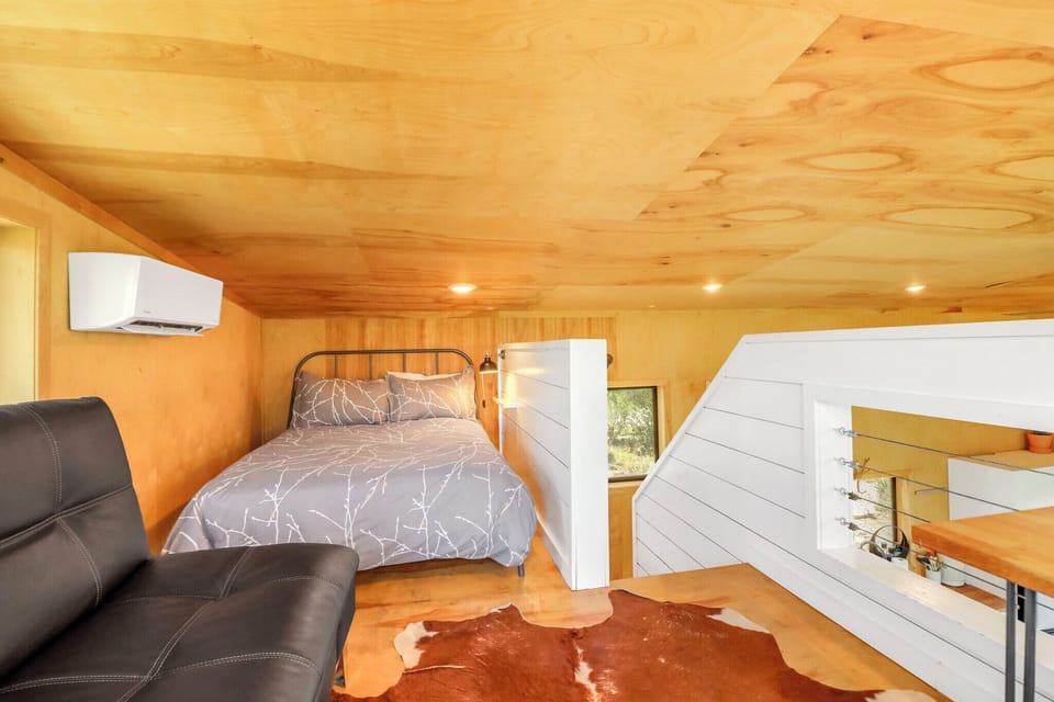 Your cozy loft bedroom blends warm wood tones with modern comfort, featuring a plush bed, air-conditioned space, and a unique rustic-chic design that feels both serene and stylish.